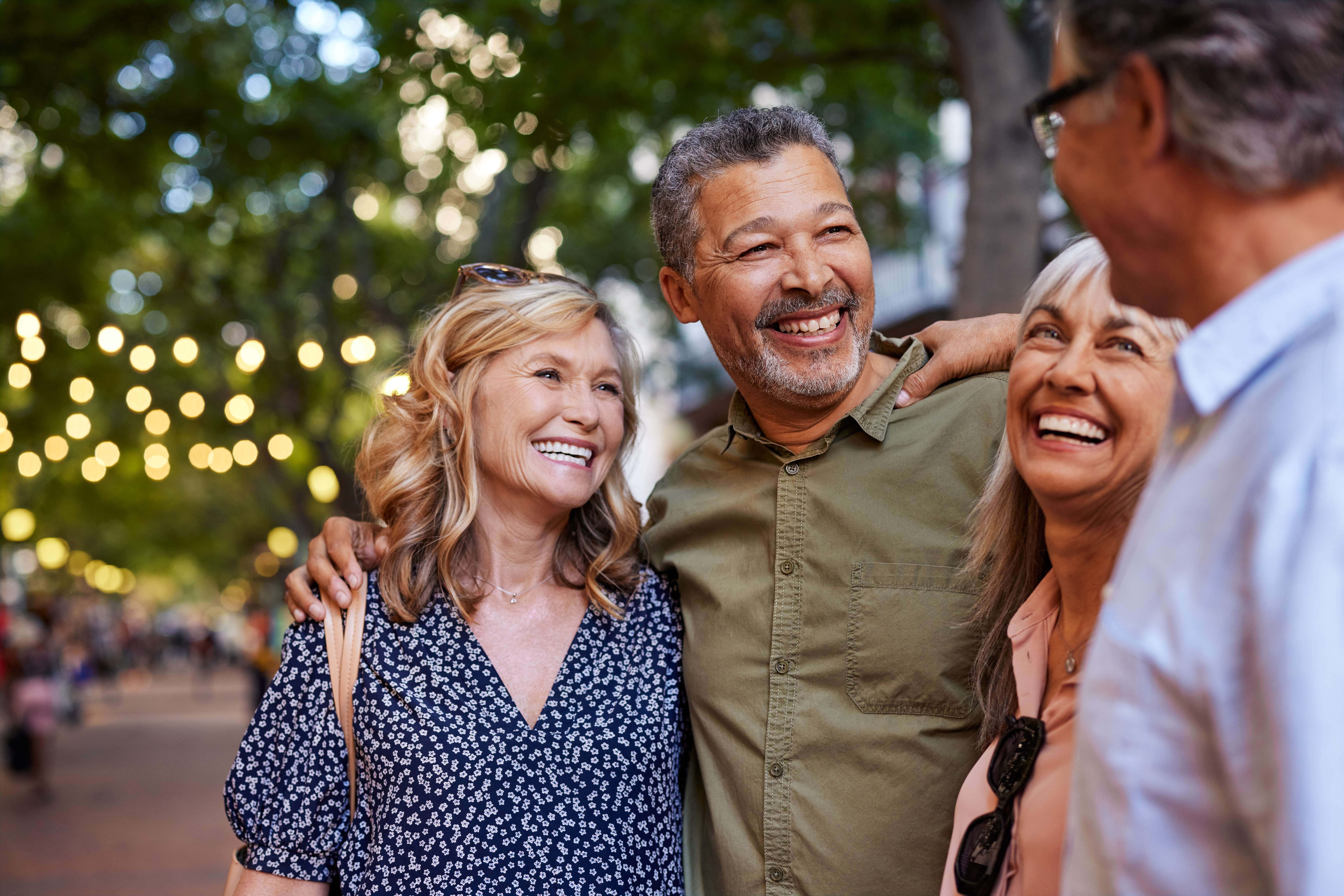 Group of happy senior friends sharing a moment outdoor while embrace. Older men and laughing women chatting together during a walk. Close up face of cheerful retirees enjoying time in a lively city street.